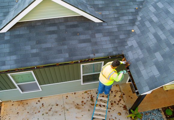 Worker is cleaning clogs in roof gutter drain by picking up dirt, debris, fallen leaves