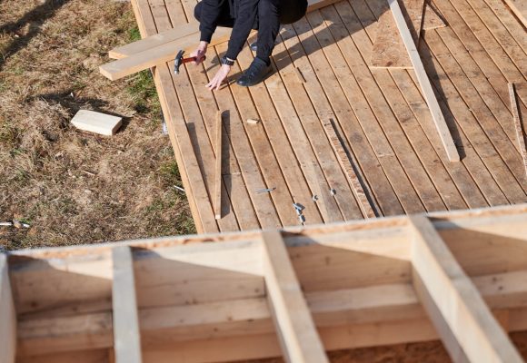 Man worker building wooden frame house. Carpenter hammering nail into wooden board, using hammer. Carpentry concept.